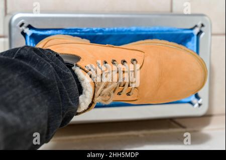 Gerät für die automatische Verkleidung von Stiefelabdeckungen, ein Mann in braunen Schuhen legt Stiefelabdeckungen, mechanische clintoper an. Stockfoto