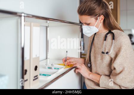 Arzt in schützender Gesichtsmaske Unterzeichnung Immunisierungszertifikat in der Mitte Stockfoto