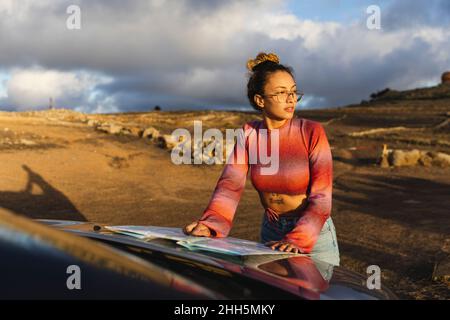 Frau mit Karte auf Autohaube bei Sonnenuntergang Stockfoto