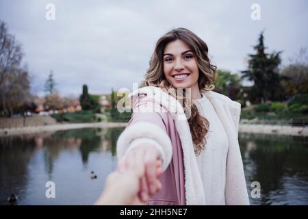 Lächelnde Frau, die die Hand des Freundes am See hält Stockfoto