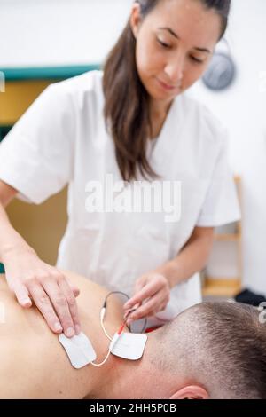 Physiotherapeut, der Elektroden am Hals des Sportlers anführt Stockfoto