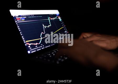 Geschäftsmann, der nachts im Heimbüro Kryptowährung auf einem Laptop verhandelte Stockfoto