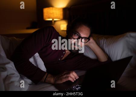 Händler mit Laptop, der nachts auf dem Bett liegt Stockfoto