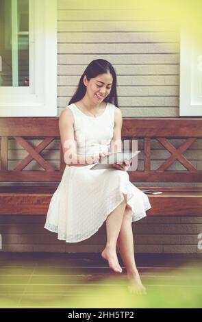 Asiatische junge Frau mit digitalen Tablet draußen auf zu Hause Sommer. Aktiver Lebensstil glücklicher junger Erwachsener an einem entspannenden Tag zu Hause. Vintage-Ton. Stockfoto