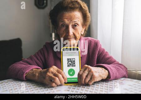 Ältere Frau mit COVID-19-Impfpass auf dem Smartphone zu Hause Stockfoto