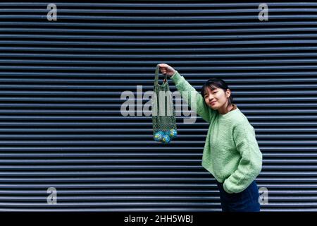 Frau, die kleine Globen in einem Netzbeutel an einer Wellwand hält Stockfoto