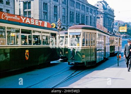 Straßenbahnen auf der Linie 9 auf dem Kornhausplatz in Bern, Schweiz c. 1960. Eine Straßenbahn wirbt für Yaset-Zigaretten. Hinter den Straßenbahnen ist der Gipfel des Kindlifresserbrunnens (‘Brunnen des Essers der Kleinen Kinder’) zu sehen. Diese Gegend ist jetzt zur Fußgängerzone erklärt worden und es gibt keine Autos, aber die Straßenbahnen fahren immer noch die Straße hoch und runter. Das Berner Straßenbahnnetz wurde 1890 in Betrieb genommen – heute hat es fünf Linien. Bern (Bern) ist die de facto Hauptstadt der Schweiz. Dieses Bild stammt von einer Amateur-35mm-Farbtransparenz – einem Vintage-1950s/1960s-Foto. Stockfoto