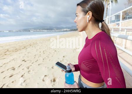 Sportlerin mit Flasche und Smartphone am Strand Stockfoto