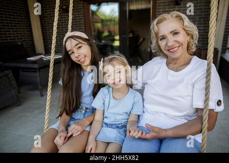 Lächelnde Großmutter mit Enkelinnen, die auf einer Seilschaukel sitzen Stockfoto