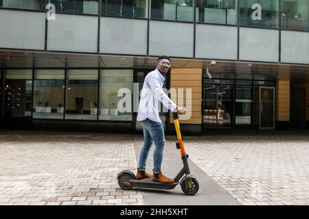 Junger Mann Reiten Elektro-Roller auf Fußpfad Stockfoto
