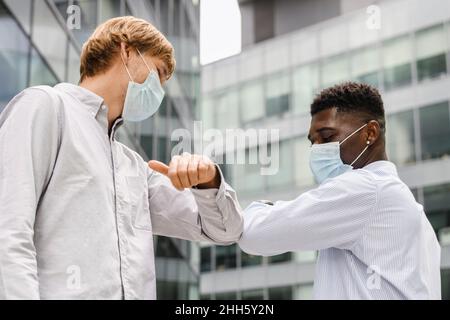 Multirassische Freunde mit chirurgischer Maske tun Ellenbogenstoß Stockfoto