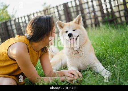 Verspielte Frau, die Akita auf Gras sitzend ansieht Stockfoto