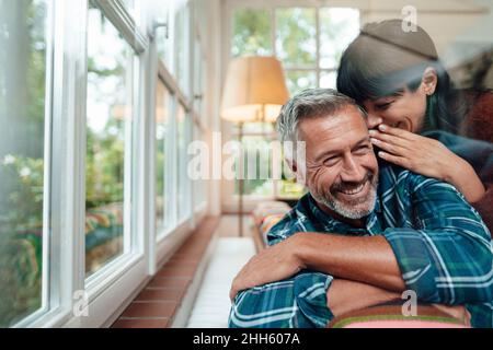 Glückliche Frau flüstert zu Hause in das Ohr des Mannes Stockfoto