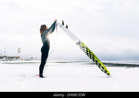 Mann probiert am verschneiten Strand Seil auf dem Surfbrett Stockfoto