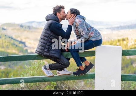 Liebevolles Paar küsst sich gegenseitig auf dem Geländer sitzend Stockfoto