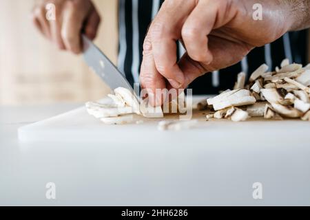 Mann schneidet Pilz mit Küchenmesser auf Schneidebrett zu Hause Stockfoto