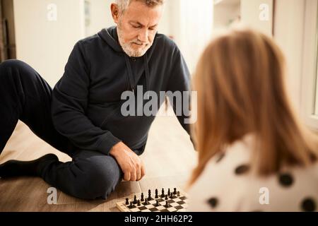 Großvater spielt Schach mit Enkelin, die zu Hause sitzt Stockfoto