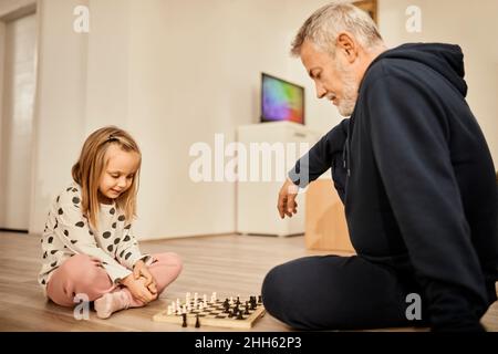 Enkelin und Großvater spielen zu Hause Schach Stockfoto