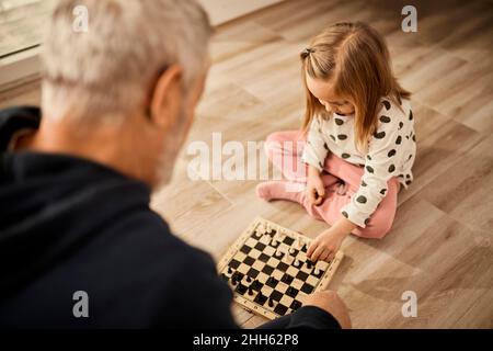 Enkelin spielt Schach mit Großvater, der zu Hause sitzt Stockfoto