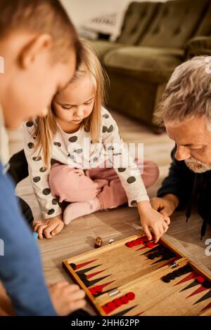 Mädchen, das Backgammon mit Großvater zu Hause lernt Stockfoto