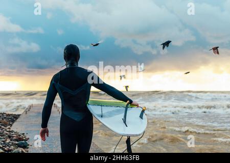 Surfer zu Fuß mit Surfbrett auf dem Pier in Richtung Meer Stockfoto