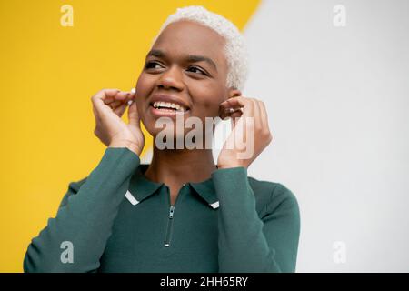 Lächelnde Frau mit in-Ear-Kopfhörern vor der Wand Stockfoto
