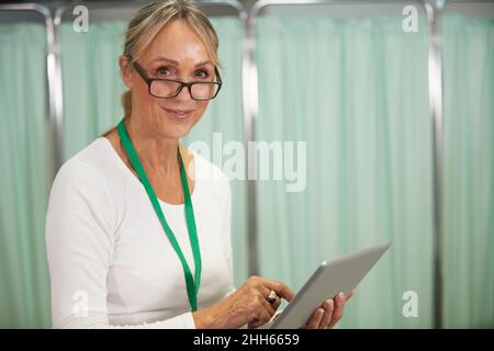 Lächelnde Ärztin mit Brillen, die den Tablet-PC im medizinischen Raum halten Stockfoto