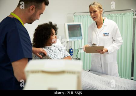 Ärztin im Gespräch mit Krankenschwester, die den Blutdruck des Patienten im Krankenhaus untersucht Stockfoto