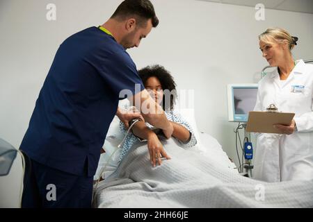 Krankenschwester, die den Patienten beim Tragen eines Blutdruckmessgeräts auf der Krankenhausstation unterstützt Stockfoto