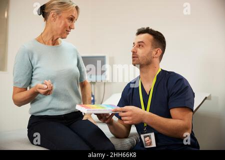 Krankenschwester mit Medikamentenkiste und Gespräch mit dem Patienten im medizinischen Raum Stockfoto