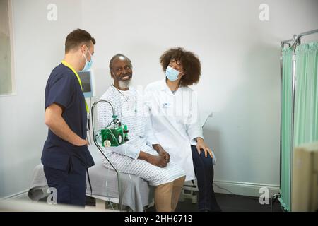 Lächelnder Patient mit Arzt, der die Krankenschwester im medizinischen Raum ansieht Stockfoto