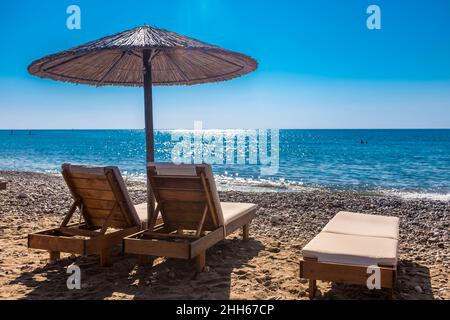 Leere Liegestühle am Küstenstrand mit klarer Horizonterlinie über dem Meer im Hintergrund Stockfoto