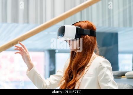 Rothaarige Frau, die im Büro mit einem Virtual-Reality-Headset arbeitet Stockfoto