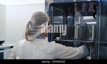 Medizinische virologische Forscherin arbeitet mit Maske. Clip. Wissenschaftler nimmt Reagenzgläser aus dem Kühlschrank. Sie arbeitet in einer Forschungseinrichtung. Stockfoto