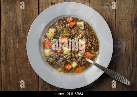 Dampfende Linsensuppe auf einem Teller mit einem Löffel auf Holzboden Stockfoto