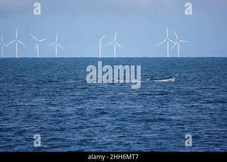 Eine Windfarm am Horizont mit einem kleinen offenen Boot, das vor dem Hotel vorbeifährt Stockfoto