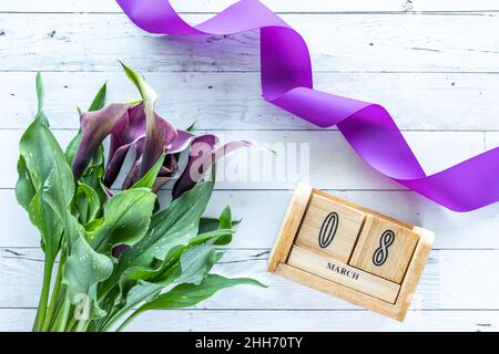 Violetter Blumenstrauß von Cala Lily und ein Datumsblock für den Internationalen Frauentag. Stockfoto