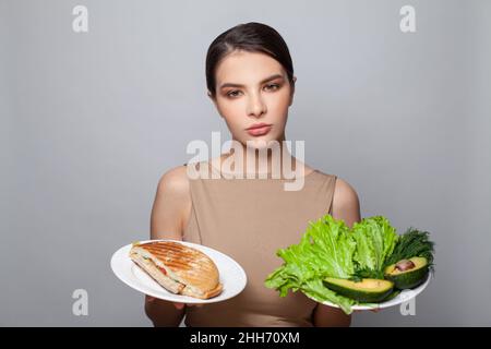 Frau hält in der Hand Sandwich und Gemüse wählen, versuchen, der Versuchung zu widerstehen, die richtige Ernährungsentscheidung zu treffen Stockfoto