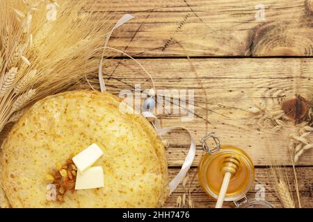 Stapel von hausgemachten frittierten Crepes, Glas mit Honig, Garbe aus Weizen und Roggen und Dekoration auf einem Holztisch mit Kopieplatz. Russische nationale Küche. Maslen Stockfoto