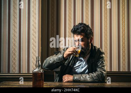 Verärgert Mann Trinker Alkoholiker mit Glas trinken Whisky allein, traurig depressiv süchtig. Flasche und Glas Whisky. Alkoholmissbrauch durch Männer. Stockfoto