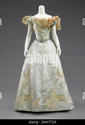 Ballkleid 1898 House of Worth French Dieses Kleid ist aus einem ganz besonderen Stoff, der à la Disposition gewebt wurde, um die Form und Abmessungen des Rockes zu passen, so dass die Schmetterlinge nach oben vom Saum flattern und, in der Größe graduiert, Scheinen in der Ferne zu verschwinden. Jean-Philippe Worth begann 1875 als Assistent seines Vaters Charles Frederick Worth. Nach und nach durfte er seine eigenen Entwürfe entwerfen und als sein Vater 1895 starb, wurde er zum Lead Designer für das Haus. Er wurde für die Herstellung von aufwendigen künstlerischen Kleidern mit komplizierten Besatz auf einzigartigen Textilien, viel lik Stockfoto