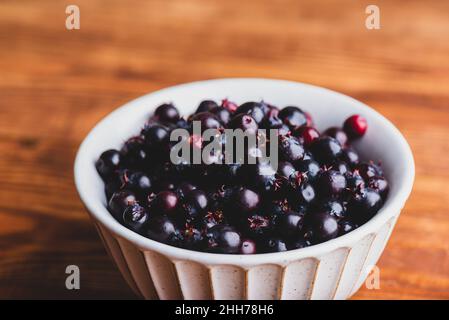 Schale voller purpurner Amelanchier Lamarckii Früchte auf rustikaler Holzoberfläche Stockfoto