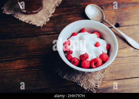 Schale Sommerdessert mit süßen Himbeeren und Joghurt auf Holzoberfläche Stockfoto