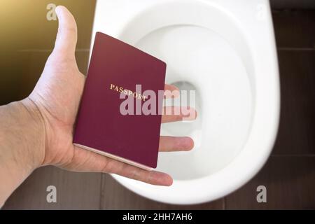 Die Hand hält den Pass des Bürgers über die Toilette und wirft seinen Pass aus. Konzept - Änderung der Staatsbürgerschaft, Verlust des Reisepasses, politische Probleme, infr Stockfoto