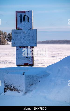 Helsinki / Finnland - JANUARU 17, 2022: Nautisches Schild, das die schneebedeckte Geschwindigkeitsbegrenzung anzeigt. Die Wintersonne wirft Schatten auf das gefrorene Meer. Stockfoto