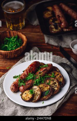 Gebackene Schweinswürste mit Auberginen und Lauch auf weißem Teller Garniert mit frischen Kräutern Stockfoto