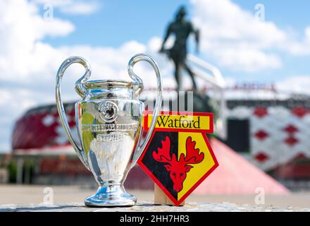 14. Juni 2021, Watford, Großbritannien. Watford FC Fußballverein-Emblem und der UEFA Champions League Cup vor der Kulisse eines modernen Stadions. Stockfoto