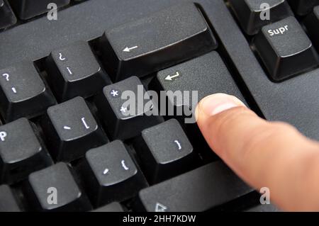 Nahaufnahme des Zeigefingers Drücken Sie die Eingabetaste auf der schwarzen Tastatur Stockfoto