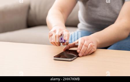 Zugeschnittene Aufnahme einer unkenntlichen Frau, die zu Hause ihr Gerät oder den Telefonbildschirm reinigt Stockfoto
