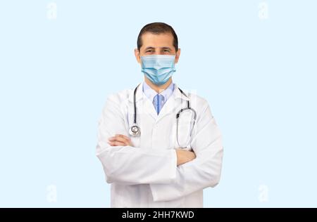 Porträt eines reifen Arztes, der vor weißem Hintergrund einen Laborkittel und eine Maske trägt Stockfoto